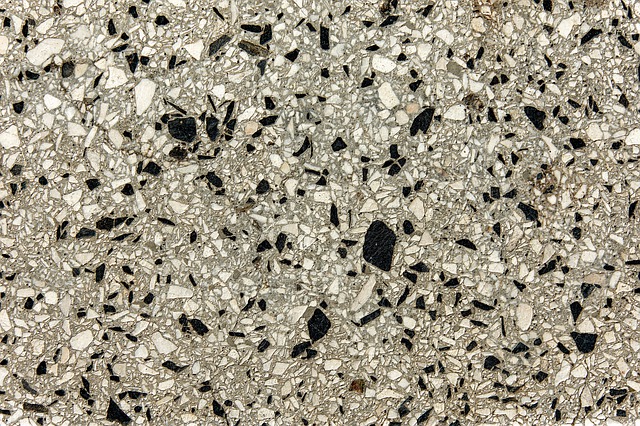 The image features a close-up view of a polished concrete surface, displaying a mixture of various-sized aggregates and pebbles embedded within the concrete. The colour palette consists of light grey shades along with black and white fragments, showcasing the decorative nature of polished concrete. This type of flooring is commonly used in both residential and commercial settings due to its durability and aesthetic appeal, making it ideal for areas such as showrooms, cafes, and modern homes. The smooth finish reflects light, enhancing the overall brightness of the space.