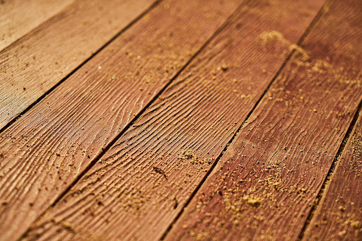 The image showcases a detailed close-up of a wooden floor surface featuring prominent grain patterns and some dust, indicative of a recent sanding or finishing. The texture of the boards highlights the quality of craftsmanship, which would appeal to potential clients looking for flooring solutions. An image like this can effectively represent AAA Floor Sanding, Concrete Polishing and Grinding's expertise in enhancing the beauty and durability of wooden floors.